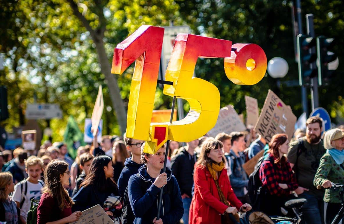 Climate change protest with demonstrator holding up three-dimensional ‘1.5°’ sign.