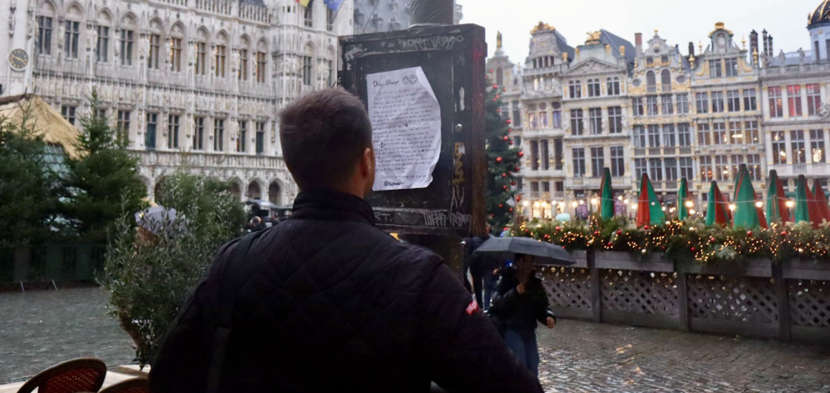 a back view of Jay, the artist of the project, hanging up one of his 'Dear Stranger' letters on a pole on the Grand Place in Brussels.